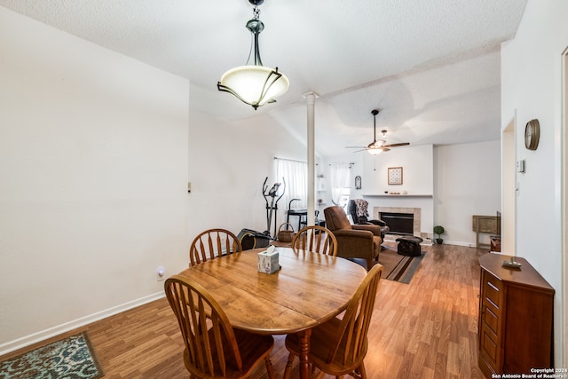 dining space featuring wood-type flooring, a textured ceiling, a tiled fireplace, ceiling fan, and vaulted ceiling