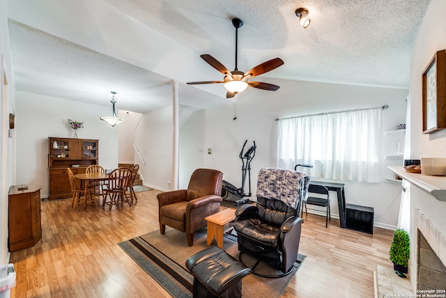 living room with vaulted ceiling, a textured ceiling, light wood-type flooring, and ceiling fan