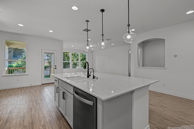 kitchen with sink, decorative light fixtures, stainless steel dishwasher, light hardwood / wood-style flooring, and a center island with sink