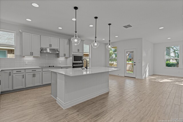 kitchen featuring a kitchen island with sink, decorative light fixtures, a healthy amount of sunlight, and stainless steel appliances