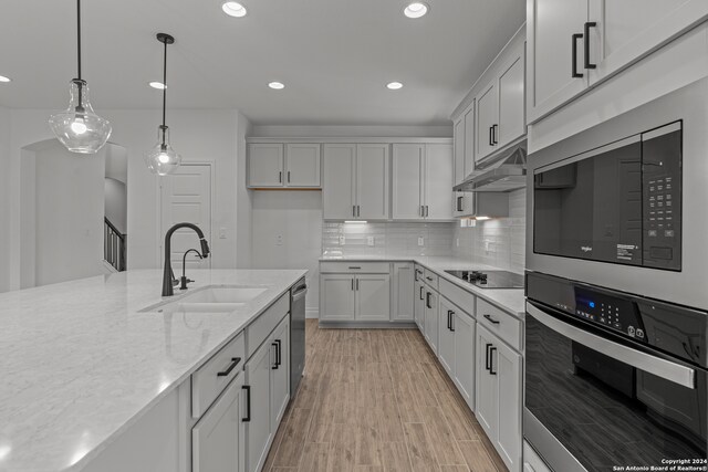 kitchen with stainless steel appliances, sink, pendant lighting, light wood-type flooring, and light stone counters