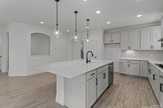 kitchen featuring an island with sink, light stone countertops, light wood-type flooring, pendant lighting, and sink