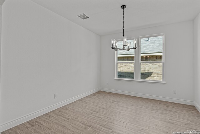 empty room featuring light hardwood / wood-style floors and a notable chandelier