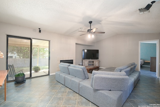 tiled living room with lofted ceiling, a textured ceiling, a tiled fireplace, and ceiling fan