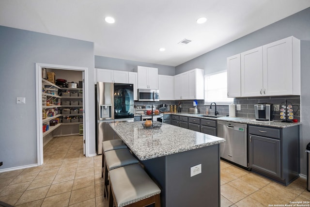 kitchen with white cabinets, light stone counters, appliances with stainless steel finishes, gray cabinetry, and a center island