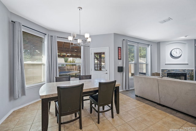 tiled dining space with a chandelier and a stone fireplace