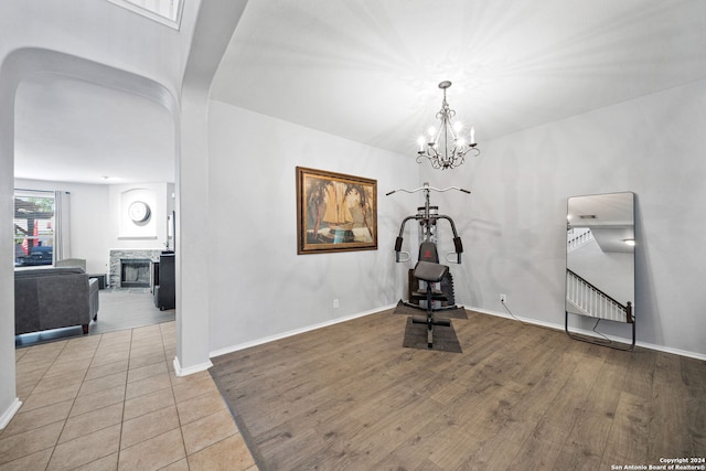 workout area with a notable chandelier, a stone fireplace, and light hardwood / wood-style flooring