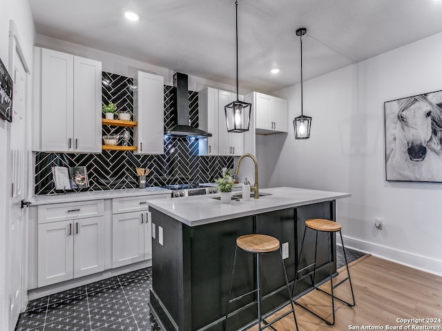 kitchen with wall chimney exhaust hood, a kitchen island with sink, hanging light fixtures, and white cabinets