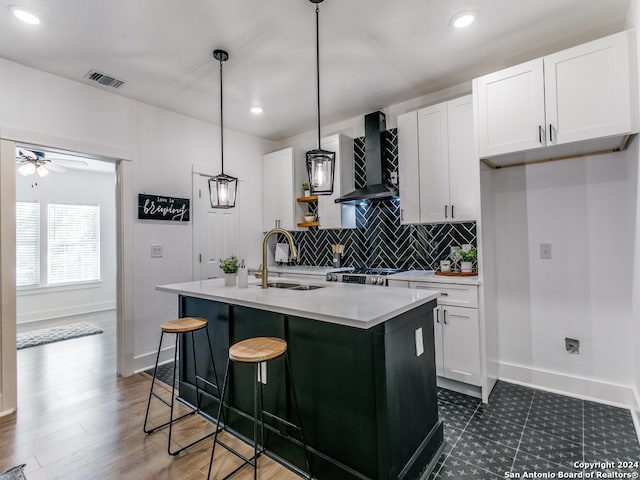 kitchen featuring sink, white cabinetry, wall chimney exhaust hood, pendant lighting, and a kitchen island with sink