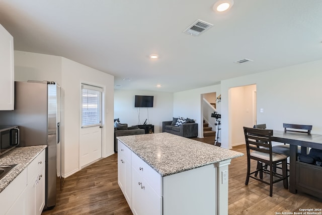 kitchen with light stone counters, appliances with stainless steel finishes, white cabinetry, dark wood-type flooring, and a center island