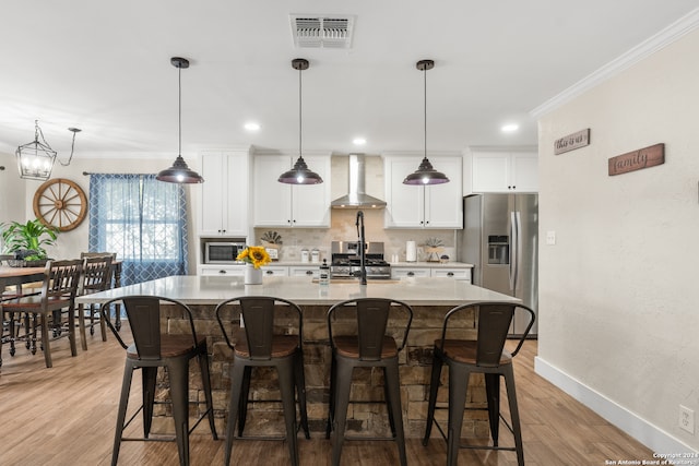 kitchen with light hardwood / wood-style floors, wall chimney exhaust hood, stainless steel appliances, and an island with sink