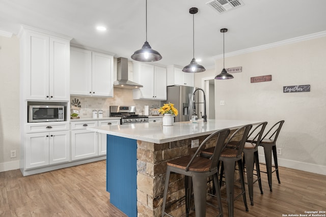 kitchen featuring appliances with stainless steel finishes, wall chimney exhaust hood, white cabinets, and a center island with sink