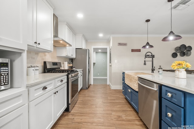 kitchen featuring hanging light fixtures, appliances with stainless steel finishes, white cabinetry, blue cabinetry, and wall chimney exhaust hood