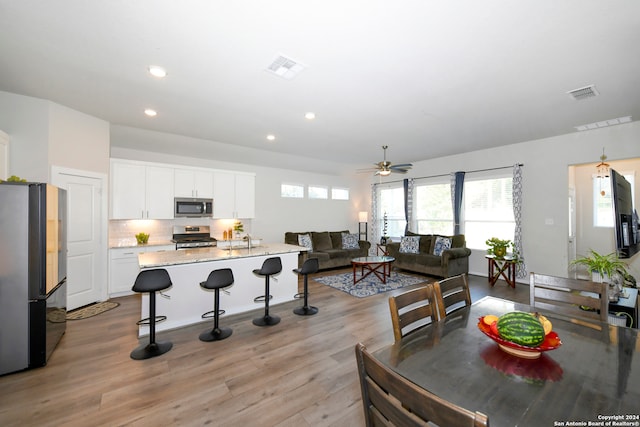 kitchen featuring light stone countertops, appliances with stainless steel finishes, light wood-type flooring, ceiling fan, and white cabinets