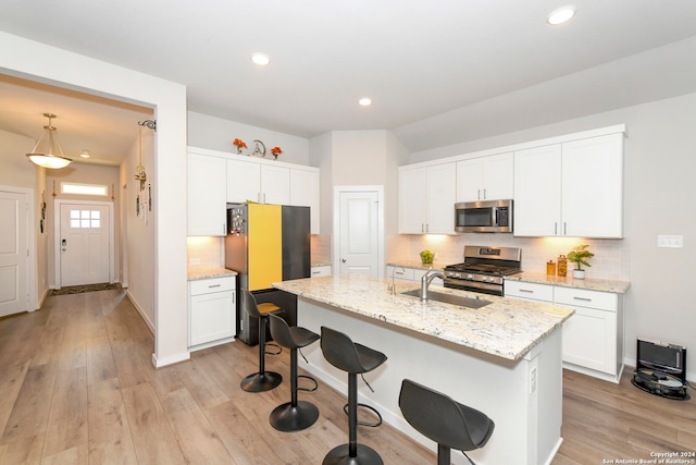 kitchen with appliances with stainless steel finishes, hanging light fixtures, white cabinetry, light hardwood / wood-style floors, and a kitchen island with sink