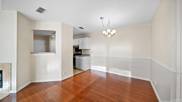 unfurnished dining area with hardwood / wood-style flooring, a textured ceiling, a notable chandelier, and a fireplace