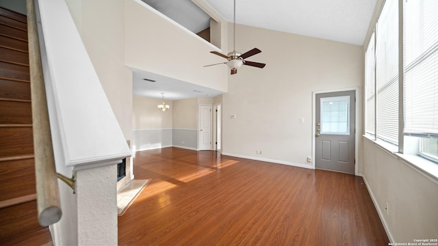 unfurnished living room featuring dark hardwood / wood-style flooring, ceiling fan with notable chandelier, and high vaulted ceiling