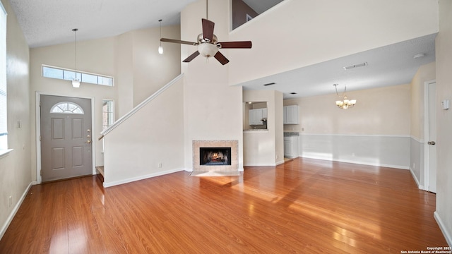 unfurnished living room with ceiling fan with notable chandelier, wood-type flooring, a textured ceiling, and a towering ceiling