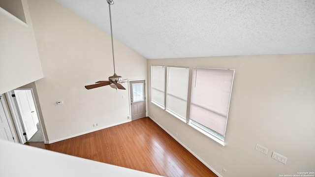 unfurnished living room with a textured ceiling, ceiling fan, vaulted ceiling, and hardwood / wood-style flooring