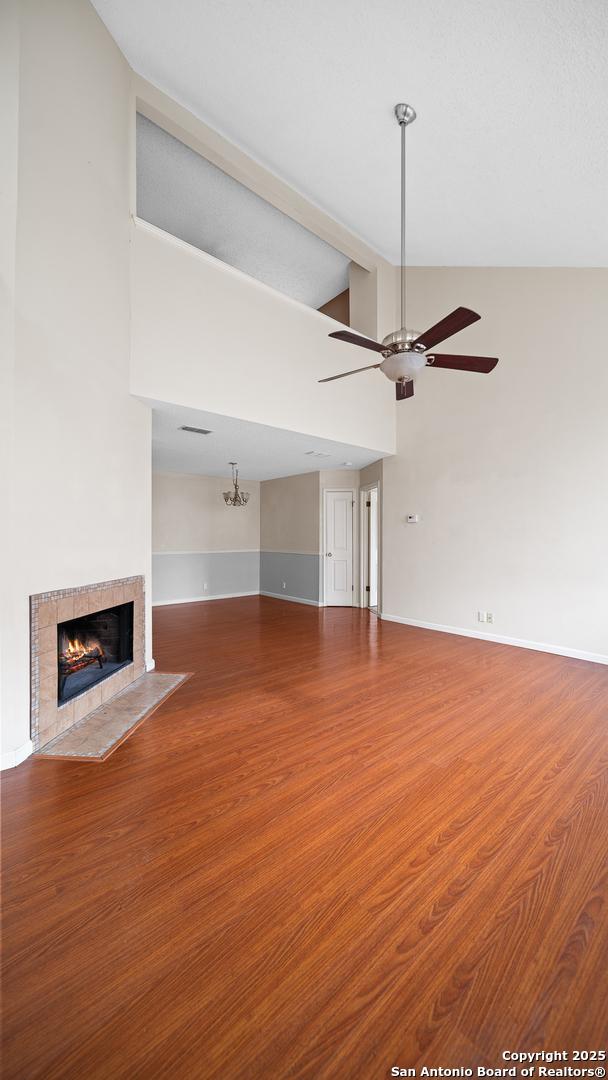 unfurnished living room featuring ceiling fan, wood-type flooring, a tile fireplace, and high vaulted ceiling