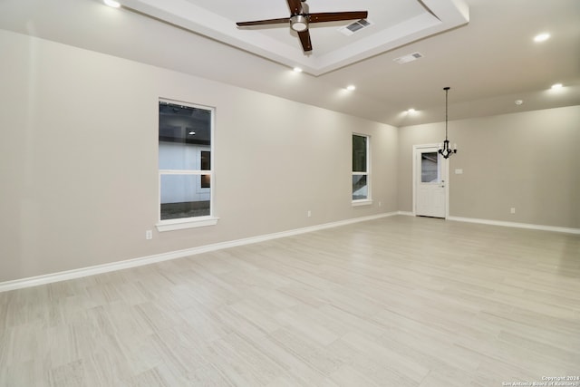 empty room with light hardwood / wood-style floors, a raised ceiling, and ceiling fan