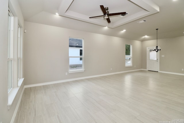 empty room with light hardwood / wood-style flooring, ceiling fan with notable chandelier, and a raised ceiling