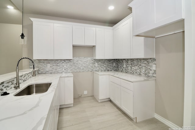 kitchen with tasteful backsplash, light stone counters, white cabinetry, sink, and decorative light fixtures