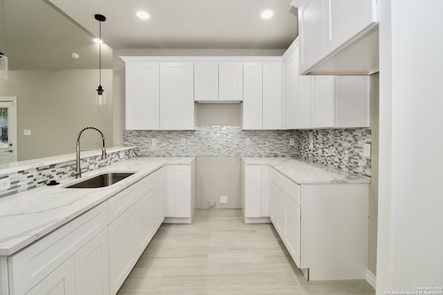 kitchen featuring backsplash, sink, decorative light fixtures, white cabinets, and light stone counters