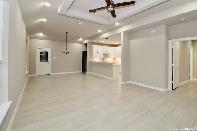 unfurnished living room featuring sink, a tray ceiling, light hardwood / wood-style floors, and ceiling fan