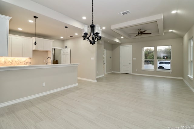 unfurnished living room with sink, light wood-type flooring, ceiling fan with notable chandelier, and a raised ceiling