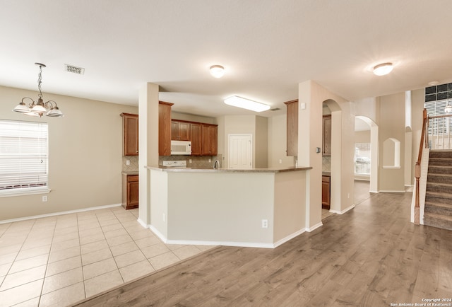 kitchen with kitchen peninsula, white appliances, a notable chandelier, light hardwood / wood-style floors, and tasteful backsplash