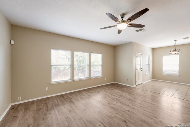 unfurnished room featuring a healthy amount of sunlight, wood finished floors, and ceiling fan with notable chandelier