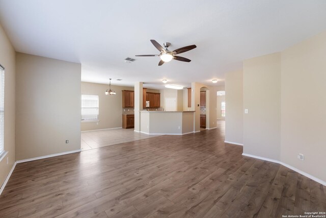unfurnished living room featuring wood finished floors, ceiling fan with notable chandelier, arched walkways, baseboards, and visible vents