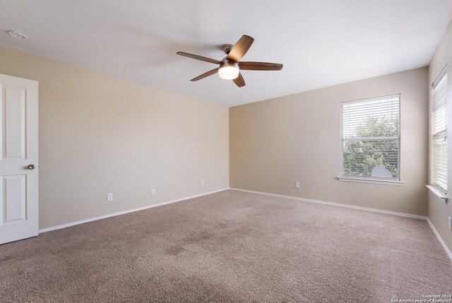 carpeted spare room featuring baseboards and a ceiling fan