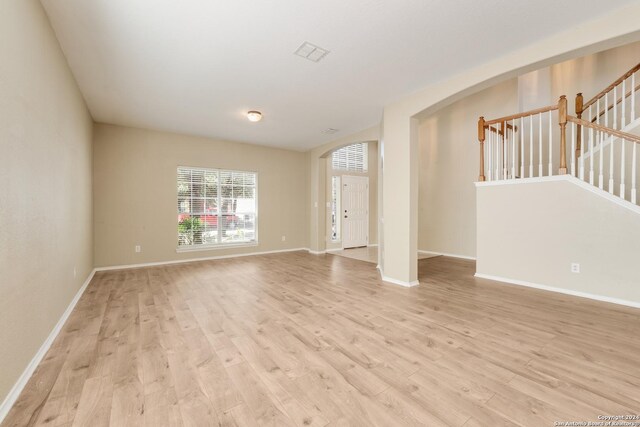 unfurnished living room with light wood finished floors, baseboards, visible vents, and arched walkways