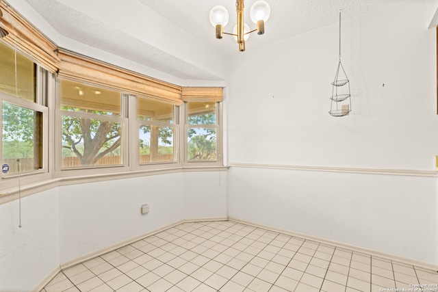 tiled empty room with a chandelier, a textured ceiling, and a healthy amount of sunlight