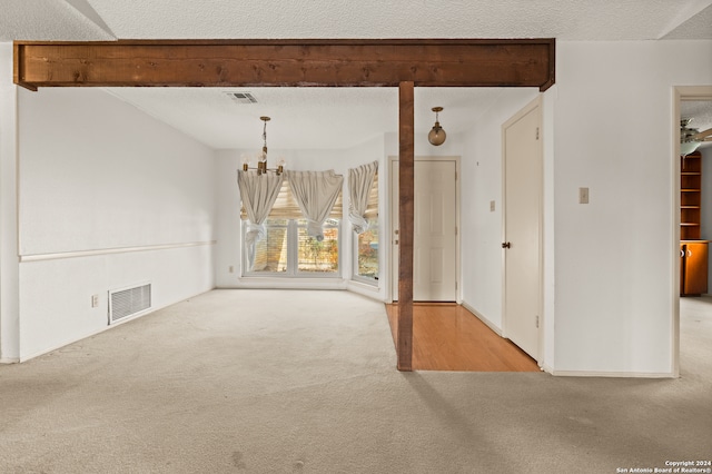 carpeted empty room with a textured ceiling, an inviting chandelier, and beamed ceiling