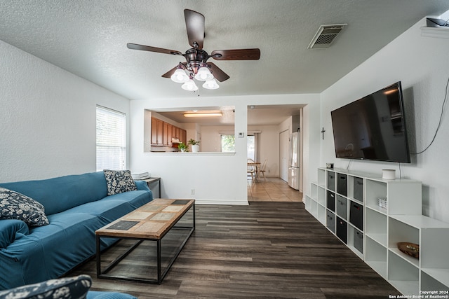 living room with ceiling fan, a healthy amount of sunlight, a textured ceiling, and dark hardwood / wood-style floors