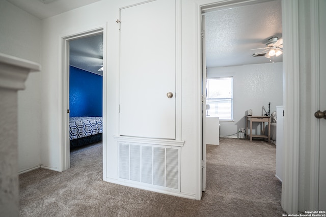 hall with a textured ceiling and light colored carpet