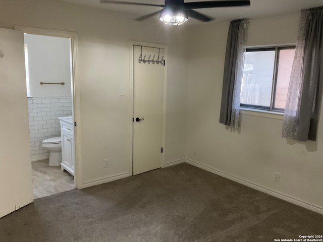 unfurnished bedroom with carpet floors, ensuite bath, tile walls, and ceiling fan