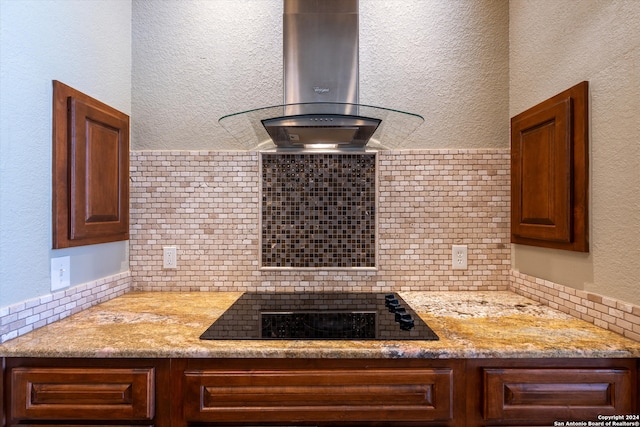 kitchen featuring light stone countertops, island range hood, black stovetop, and tasteful backsplash