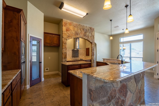 kitchen featuring a large island, a textured ceiling, light stone countertops, wall chimney exhaust hood, and decorative light fixtures