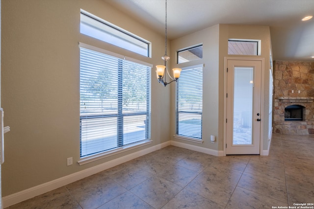 unfurnished dining area featuring a stone fireplace and an inviting chandelier