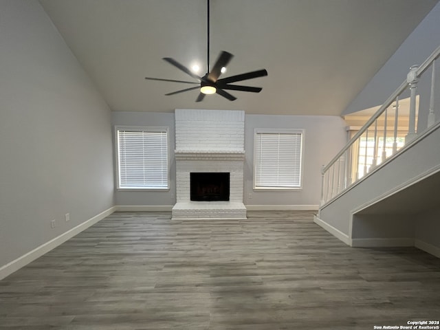 unfurnished living room featuring vaulted ceiling, a brick fireplace, wood-type flooring, and ceiling fan