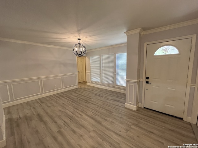 foyer entrance with crown molding, a chandelier, wood-type flooring, and ornate columns