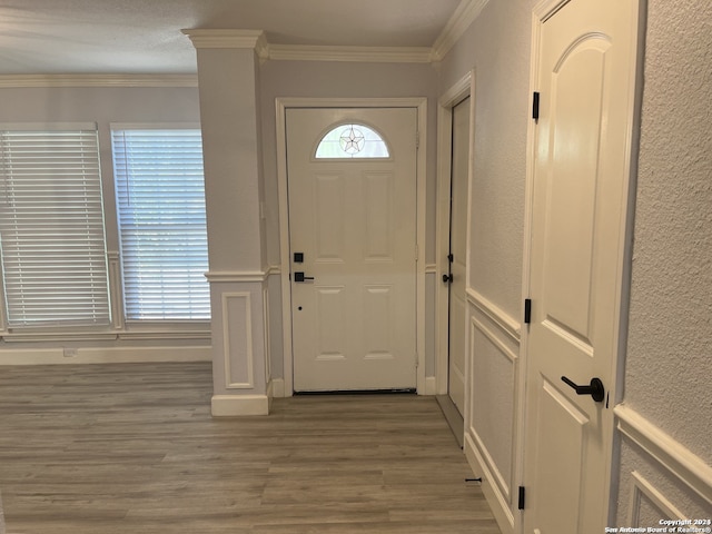 foyer entrance featuring ornamental molding, decorative columns, and wood-type flooring