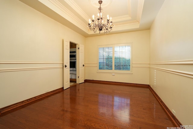 empty room with an inviting chandelier, a raised ceiling, baseboards, ornamental molding, and wood finished floors