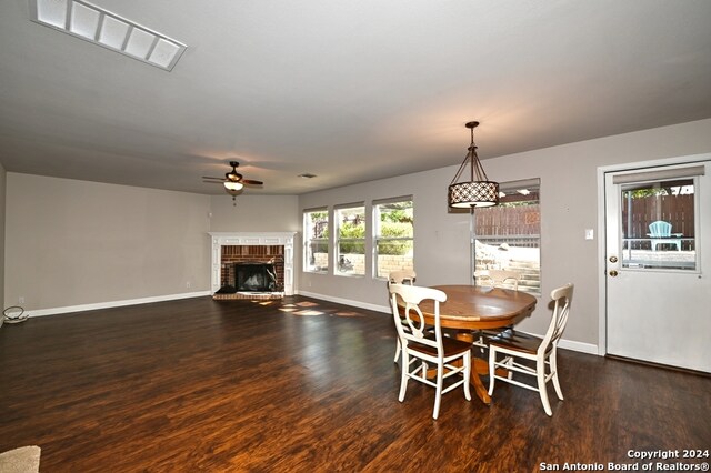 dining room with ceiling fan, a brick fireplace, and dark hardwood / wood-style flooring