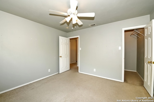 unfurnished bedroom featuring light carpet, a closet, a spacious closet, and ceiling fan