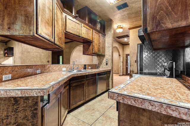 kitchen with dark brown cabinets, light tile patterned floors, a textured ceiling, dishwasher, and sink